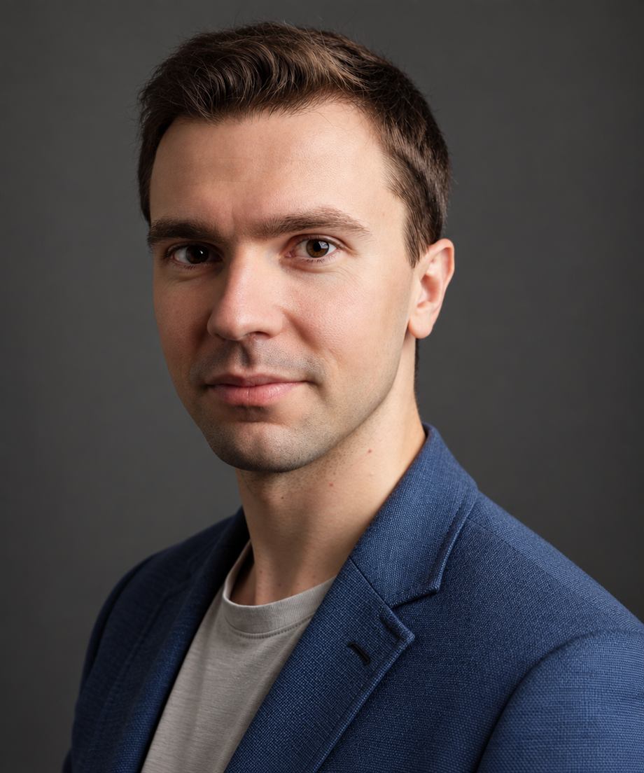 Kamil Polak, portret do piersi, w granatowej marynarce i jasnoszarej koszulce, na ciemnoszarym tle
